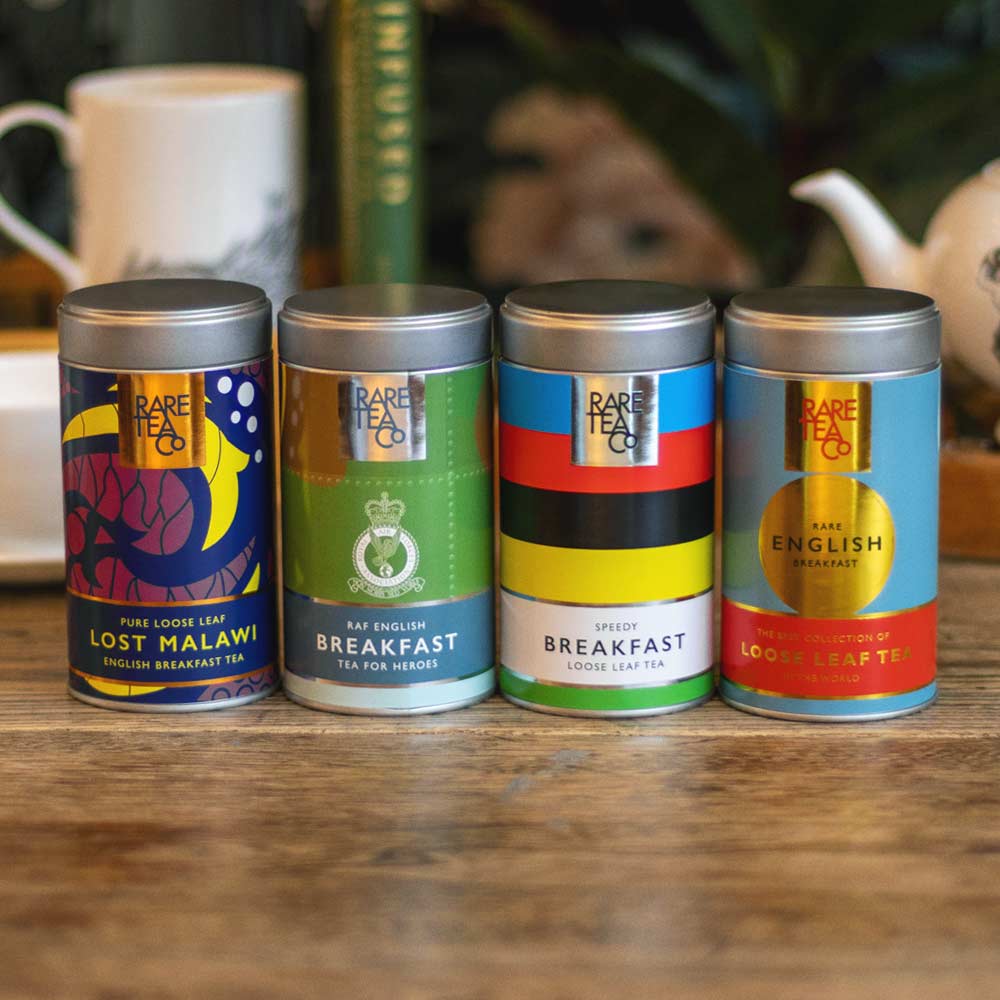 Four colourful tea tins from Rare Tea Company on a wooden surface with a blurred background.