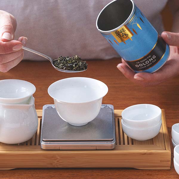 Tea-making process with a can of oolong tea, tea leaves, and teacups on a wooden tray.