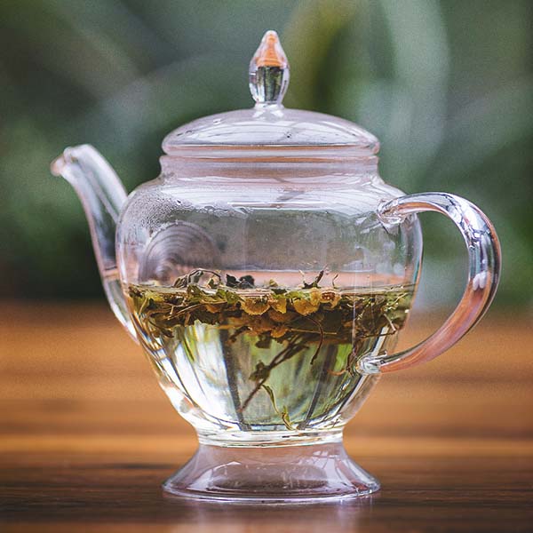 Herbal tea infusing in a clear glass teapot with on a wooden surface.