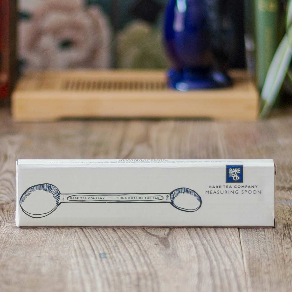 Rare Tea Co. branded measuring spoon packaging set on a wooden surface with blurred background.